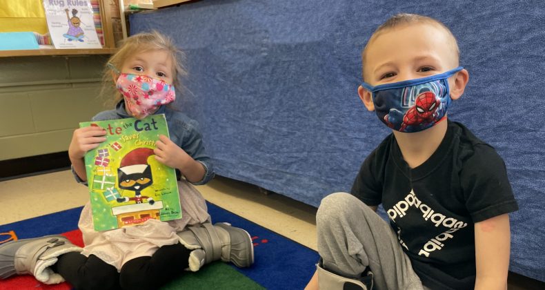 two young students sitting on classroom floor with masks on