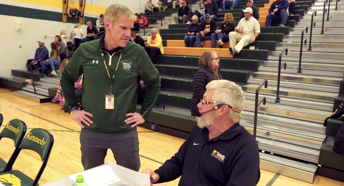 Aaron Stecker talks with the public address announcer during halftime of a basketball game.