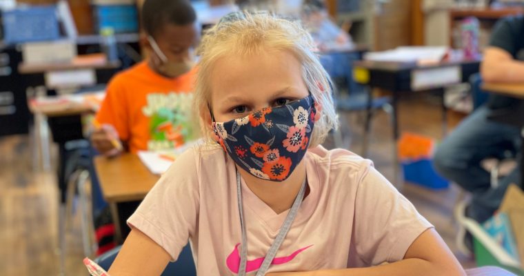 young student wearing mask looking up from desk