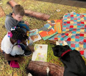 Two students read books with a dog that is laying beside them.