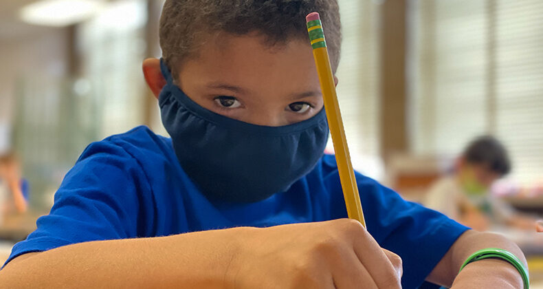 student wearing mask writing with pencil