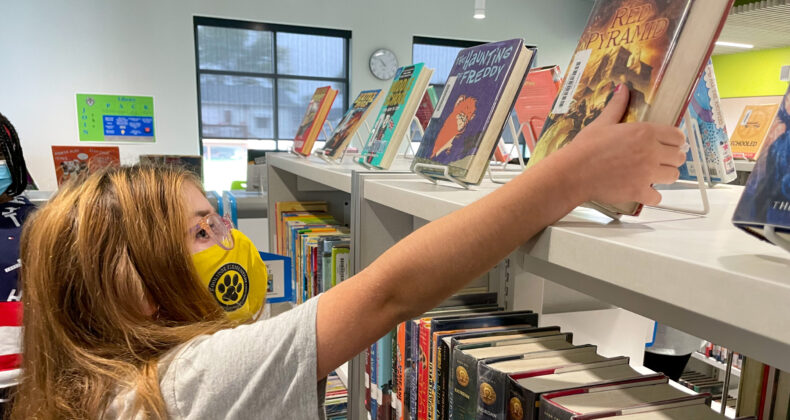 Student in library reaching for book