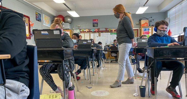 teacher walking around to students sitting at desks in classroom