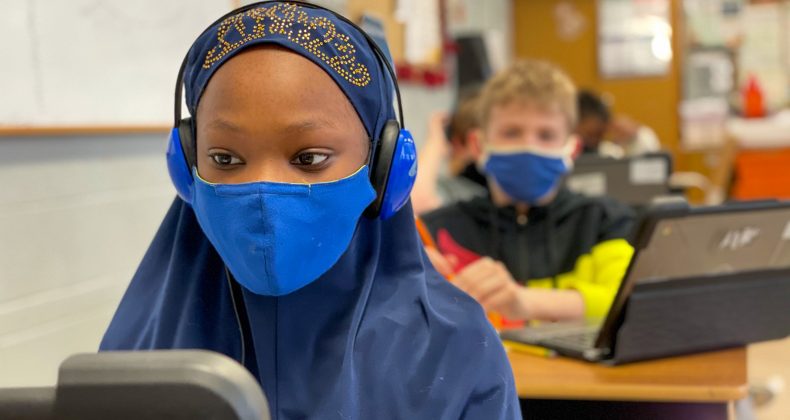 student wearing mask and headphones while looking at laptop