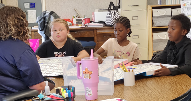 Students work with a teacher at a table.