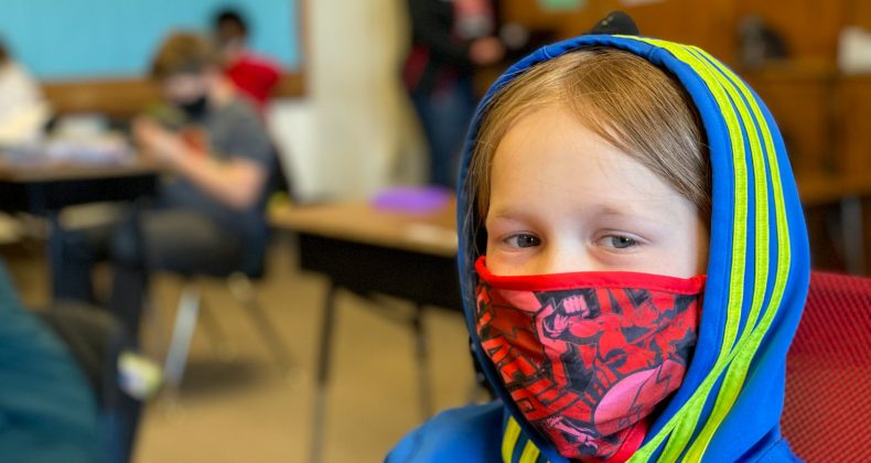 student wearing mask sitting at desk in classroom