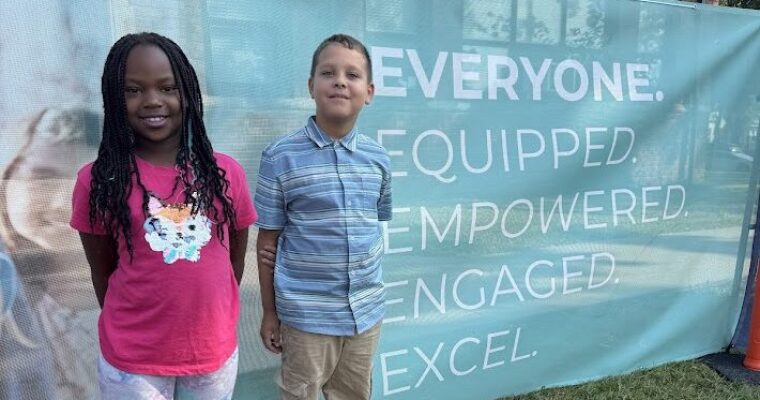 two students standing in front of the cedar rapids community school district banner at Harrison Groundbreaking