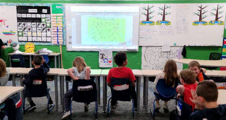 Students sitting at tables facing a projector and screen.