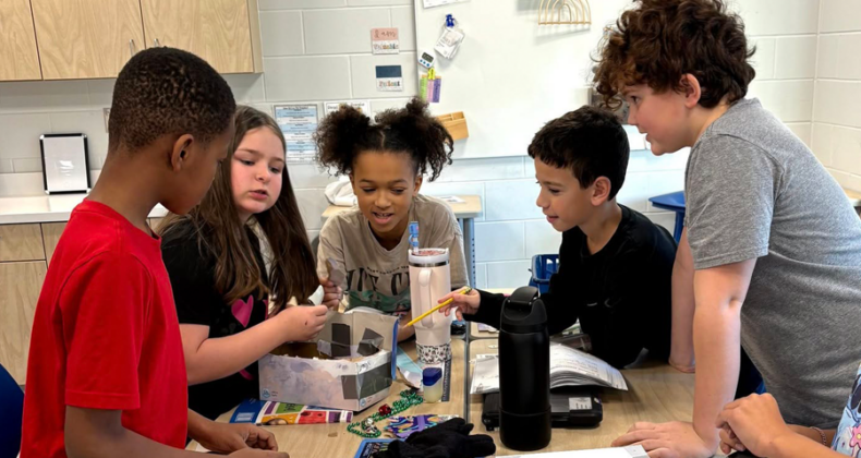 Maple Grove students work around a table on a project.