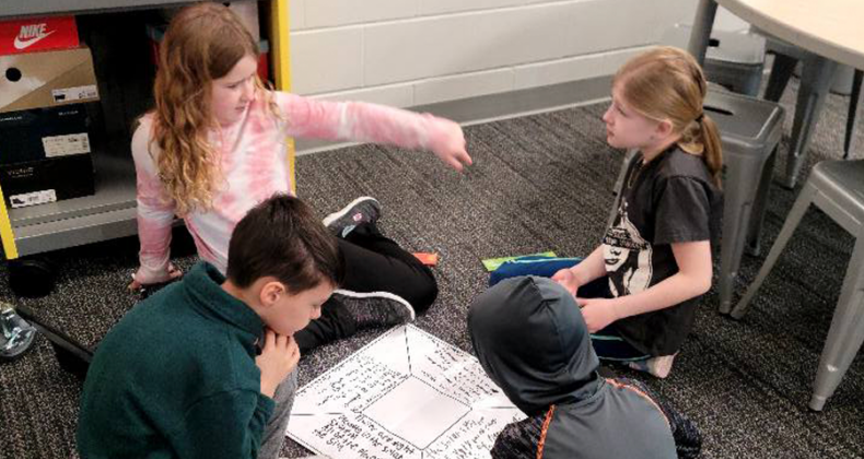 Four Maple Grove students work on a diagram to discuss their learning.