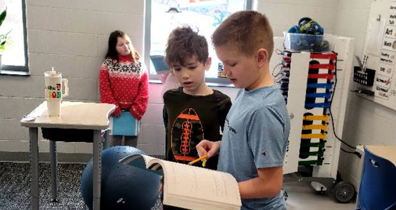 Two Maple Grove students work together, while standing in a classroom.