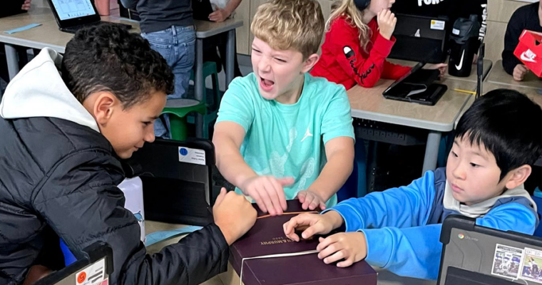 A group of three Maple Grove students work on a project. One student has excitement on their face.