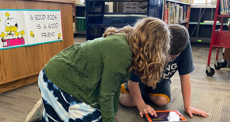 Students using personal device on floor of library