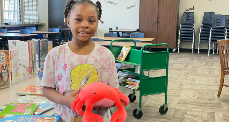 student standing in library smiling holding stuffed crab