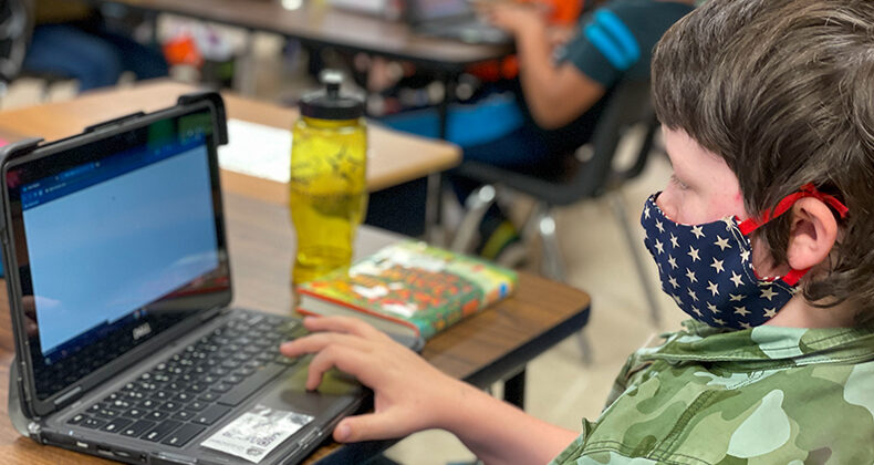 student looking at laptop wearing mask at desk