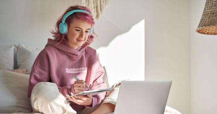 Hipster teen girl student with pink hair watch online webinar learning in bed.