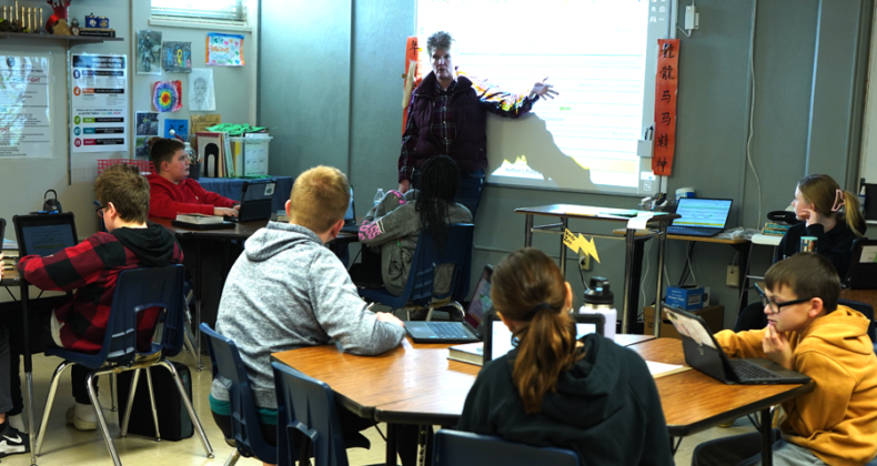 A Harding teacher points at a whiteboard as students sit listening.