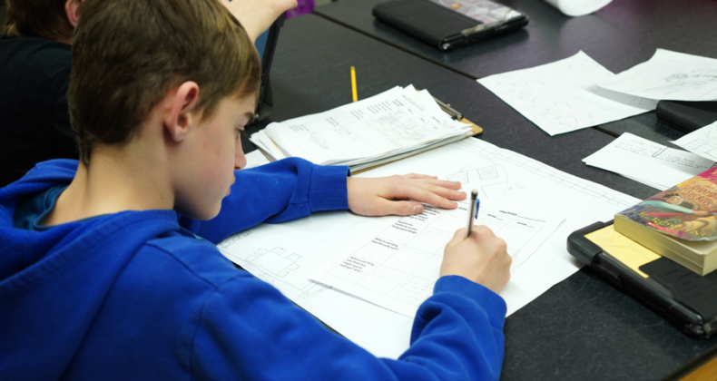 A Harding student wearing a blue sweatshirt work on a piece of paper at a table.