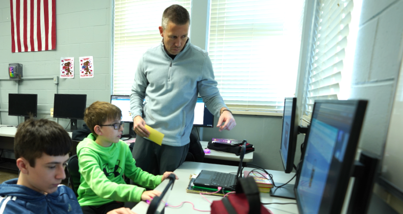 A Harding teacher works with two students in front of computers.