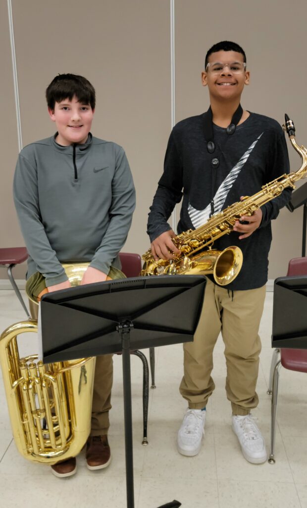 Two band students pose for a picture. A tuba player and a tenor saxophone player. 